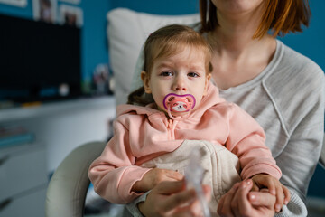 One girl little caucasian child toddler sitting with her mother use nose snot sucker nasal aspirator cleaning nose suck out snivel to release breathing cry refuse scared copy space