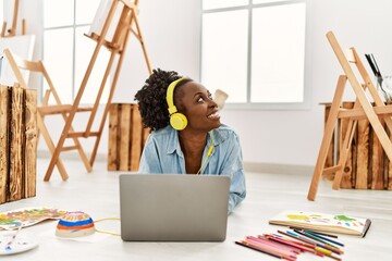 Wall Mural - Young african american artist woman using laptop and headphones at art studio.