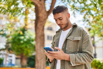 Wall Mural - Young hispanic man smiling confident using smartphone at park