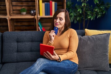 Sticker - Middle age woman using laptop and credit card sitting on sofa at home