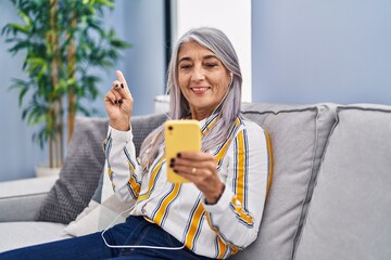 Sticker - Middle age woman with grey hair using smartphone sitting on the sofa smiling happy pointing with hand and finger to the side