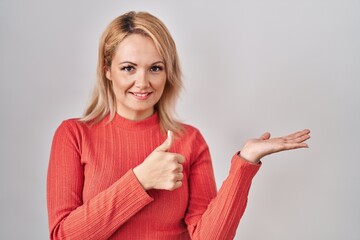 Canvas Print - Blonde woman standing over isolated background showing palm hand and doing ok gesture with thumbs up, smiling happy and cheerful