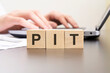 pit - acronym from wooden blocks with letters. background hands on a laptop with blur. business concept.