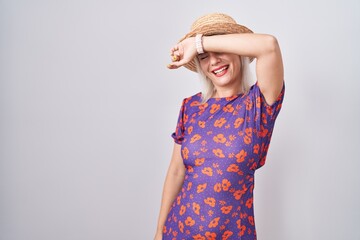 Poster - Young caucasian woman wearing flowers dress and summer hat covering eyes with arm smiling cheerful and funny. blind concept.