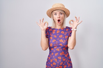 Poster - Young caucasian woman wearing flowers dress and summer hat looking surprised and shocked doing ok approval symbol with fingers. crazy expression