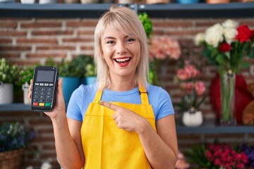 Poster - Young caucasian woman working at florist shop holding dataphone smiling happy pointing with hand and finger