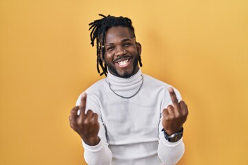 Poster - African man with dreadlocks wearing turtleneck sweater over yellow background showing middle finger doing fuck you bad expression, provocation and rude attitude. screaming excited