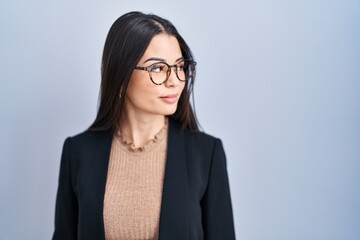 Poster - Young brunette woman standing over blue background looking to side, relax profile pose with natural face with confident smile.