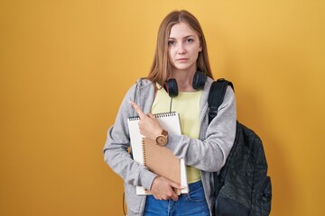 Canvas Print - Young caucasian woman wearing student backpack and holding books pointing aside worried and nervous with forefinger, concerned and surprised expression