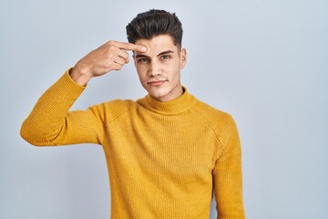 Sticker - Young hispanic man standing over blue background pointing unhappy to pimple on forehead, ugly infection of blackhead. acne and skin problem