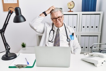 Sticker - Senior caucasian man wearing doctor uniform and stethoscope at the clinic confuse and wondering about question. uncertain with doubt, thinking with hand on head. pensive concept.