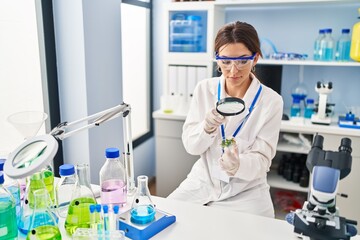 Canvas Print - Young hispanic woman wearing scientist uniform using magnifying glass at laboratory