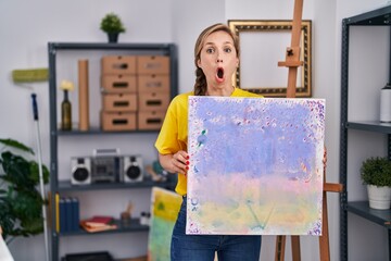 Sticker - Young blonde woman holding canvas afraid and shocked with surprise and amazed expression, fear and excited face.