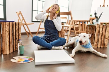 Poster - Young caucasian woman listening to music with dog at art studio