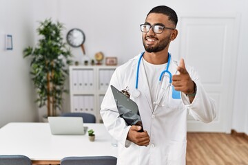 Wall Mural - Young indian man wearing doctor uniform and stethoscope pointing fingers to camera with happy and funny face. good energy and vibes.