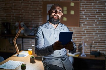 Wall Mural - Young hispanic man with beard and tattoos working at the office at night with a happy and cool smile on face. lucky person.