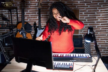 Poster - Plus size hispanic woman playing piano at music studio smiling looking to the camera showing fingers doing victory sign. number two.