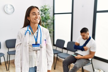 Canvas Print - Young asian doctor woman at waiting room with a man with a broken arm looking away to side with smile on face, natural expression. laughing confident.