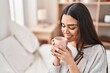 © Krakenimages.com - Young hispanic woman drinking cup of coffee sitting on bed at bedroom