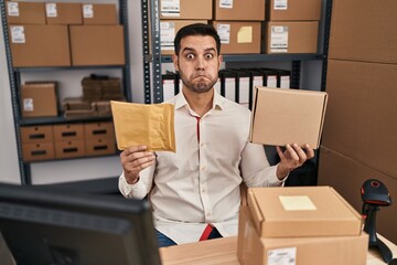 Sticker - Young hispanic man with beard working at small business ecommerce holding delivery packages puffing cheeks with funny face. mouth inflated with air, catching air.