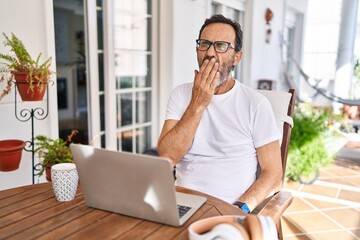 Poster - Middle age man using computer laptop at home bored yawning tired covering mouth with hand. restless and sleepiness.