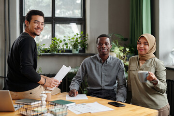 Aufkleber - Successful team of young intercultural economists in casualwear looking at camera while sitting by workplace and organizing work at meeting