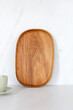 Wooden oval oak dish, board, tray standing near the wall. Empty wooden plate on kitchen white table. Empty and template mockup with place for food. Kitchen utensils.