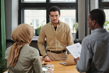 Aufkleber - Young serious manager listening to report of Muslim female subordinate while standing in front of two intercultural employees at meeting