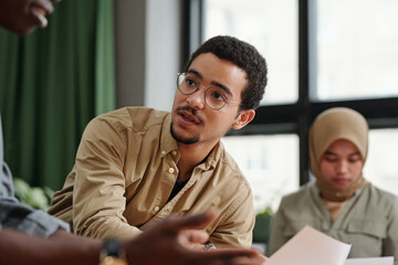 Aufkleber - Young multi-ethnic businessman in casualwear and eyeglasses talking to African American male colleague after making financial report