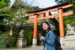 © PR Image Factory - cheerful asian Japanese girl photographer looking into distance at beautiful scenery near the red torii gate of uji jinja while traveling to Kyoto japan during spring season