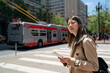 © PR Image Factory - asian taiwanese girl visitor carrying map and craning to look at distance while waiting for bus on the street with a silver red local bus at background in san Francisco California usa.