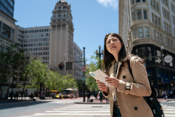 Canvas Print - curious asian Japanese girl visitor looking around city with guide map while exploring downtown san Francisco in California usa near triangular office building on sunny day