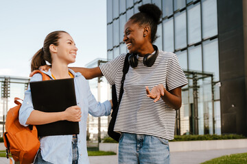 Wall Mural - Young multiracial women smiling and hugging at city street