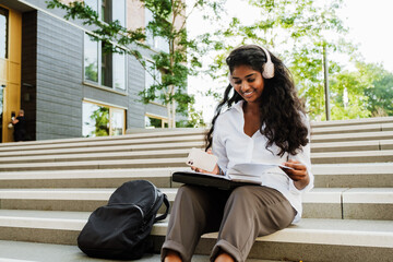 Wall Mural - Young woman using cellphone and headphones while studying outdoors