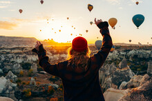 A Girl In A Red Hat And A Plaid Shirt Stands With Her Back Against The Background Of Dawn And Hot Flying Balloons