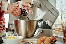 Woman In Festive Christmas Sweater Preparing Dough For Cookies At Home Kitchen. Female Hands Use Electric Mixer. Modern Kitchen Household Appliances