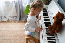 Girl Learning To Play Piano With Teddy Bear At Home