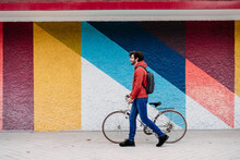 Man Wheeling With Bicycle On Footpath In Front Of Colorful Wall