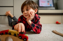 Boy Playing With Wooden Toy Train Lying On Floor At Home