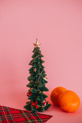 Wall Mural - A candle in the shape of a Christmas tree with gifts with a branch and two tangerines on a pink background