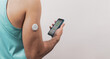 An unrecognizable man shows his defocused mobile with a continuous blood glucose test application, the patch is seen in the foreground, copy space.