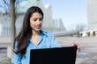 © Ana Sofía - young woman working with laptop outside with office buildings in background