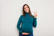 © Asier - Pregnant caucasian woman isolated on white background showing number two with fingers.