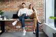 © baranq - Smiling young entrepreneurs business partners sitting together on the desk in small startup office