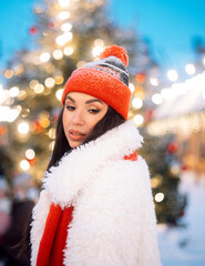 Wall Mural - Charming young woman at the Christmas market next to the New Year tree.