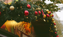 Christmas Market In Berlin, Germany. Beautiful Festive Sign On The Kiosk. Fir Branch With Red And Gold Balls, Festive Yellow Lights And Bokeh. 