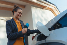 Young Woman Holding Power Supply Cable From Her Electric Car, Prepared For Charging It In Home, Sustainable And Economic Transportation Concept.
