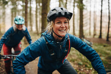 Smiling Young Woman Mountain Biking With Friends In A Forest