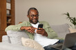 © Prostock-studio - Glad middle aged african american man in glasses reads message on phone, watches video surfing in room