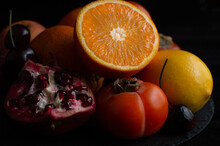 Blurred Image Of Half An Orange, Pomegranate, Persimmon, Cherry And Lemon On A Dark Background. Still Life With Fruit.